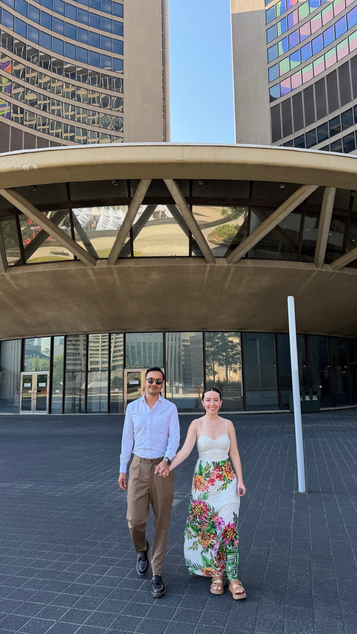 Monica and Jaime, the two founders of Fluid, walking hand in hand across a paved plaza, a curved concrete building and two towers behind them